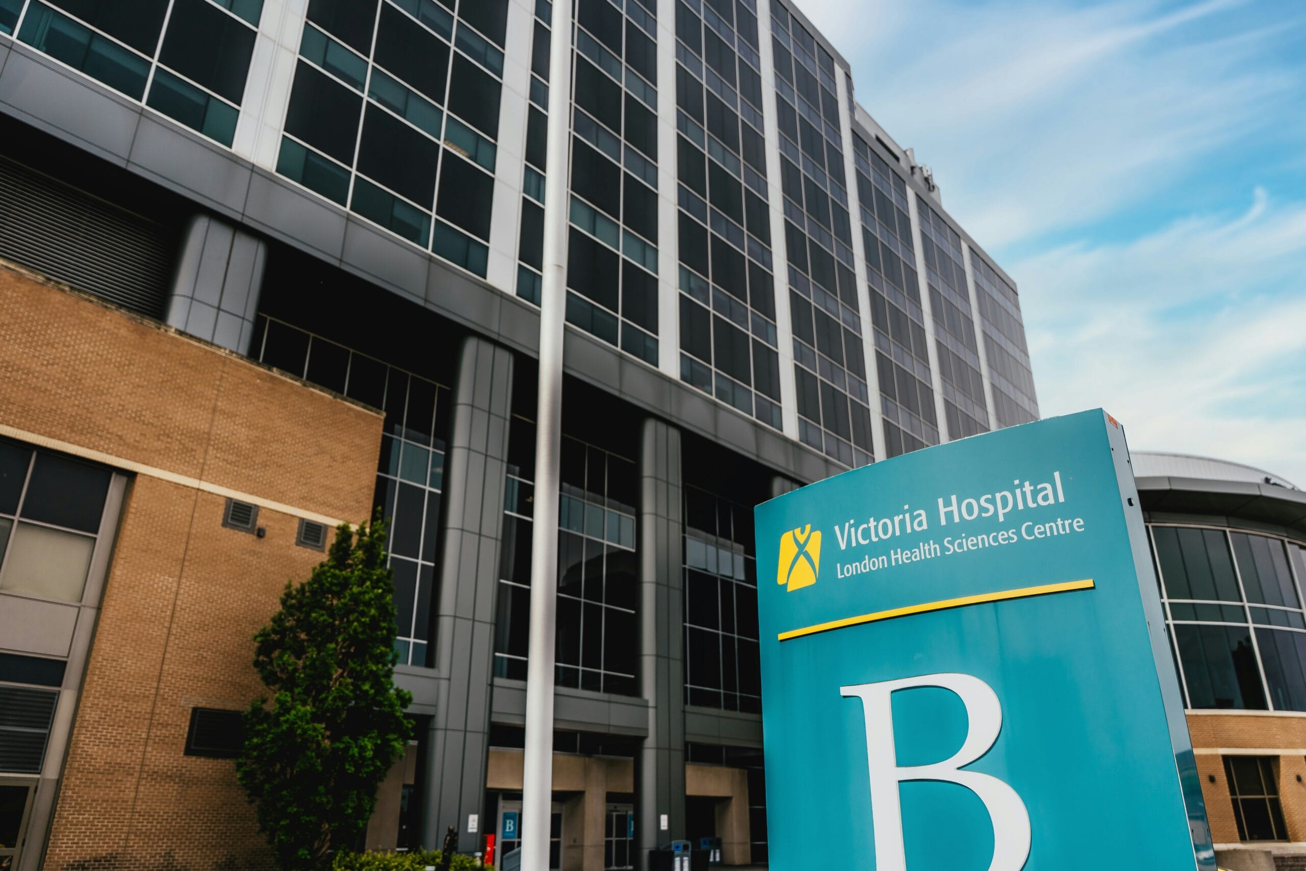 Victoria Hospital sign in front of a modern multi-story building with large windows and a clear blue sky.